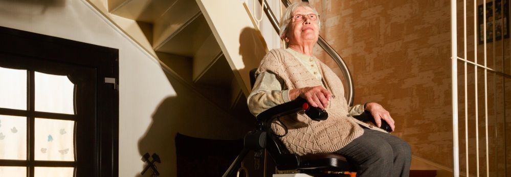 Eine ältere Person fährt mit einem Treppenlift eine Treppe hinauf.